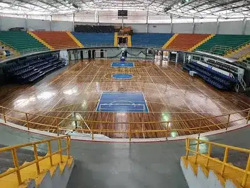 Interior del Gimnasio Nacional con la cancha de madera y las graderías de colores
